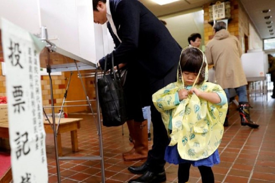 A girl stands next to her father filling out his ballot for a national election at a polling station in Tokyo, Japan October 22, 2017. Reuters