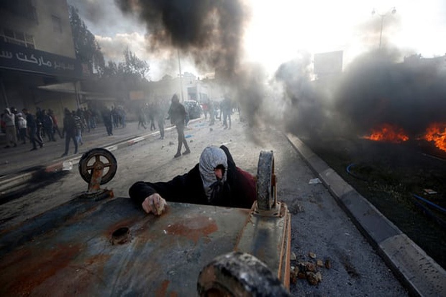 A Palestinian protester takes cover during clashes with Israeli troops in Beit El, near Ramallah. Photograph: Reuters