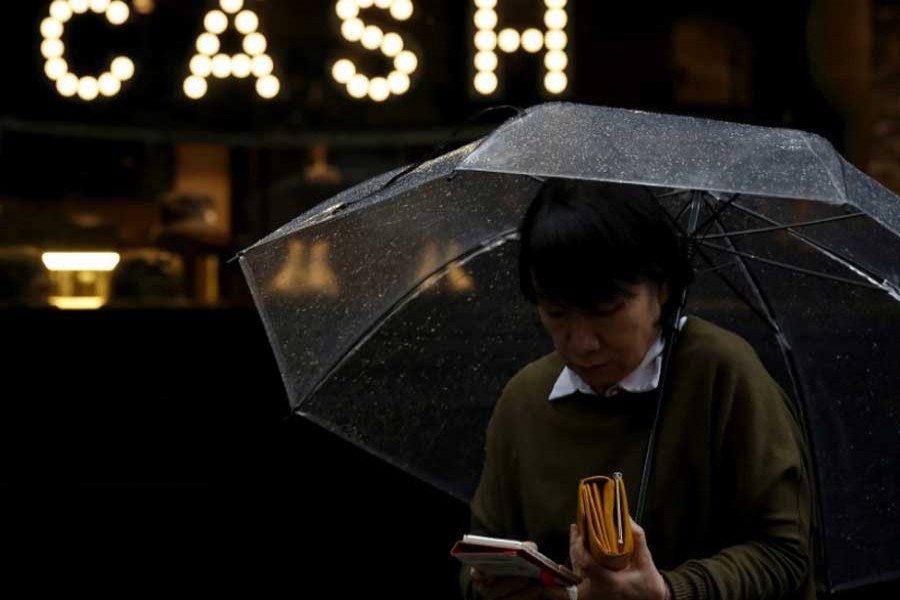 A pedestrian holding an umbrella and her wallet walks past the word "CASH", part of a sign on a street at a shopping district in Tokyo, Japan, March 7, 2016. Reuters/File Photo