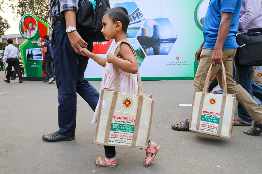 A little girl is seen with a jute-made souvenir bag given to her father by the NBR at the tax fair in Dhaka on Thursday — FE photo