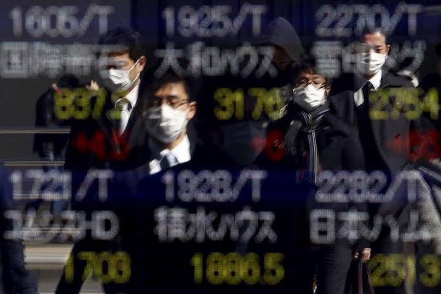 Pedestrians wearing masks are reflected in an electronic board showing various stock prices outside a brokerage in Tokyo, Japan, February 26, 2016. Reuters/Files