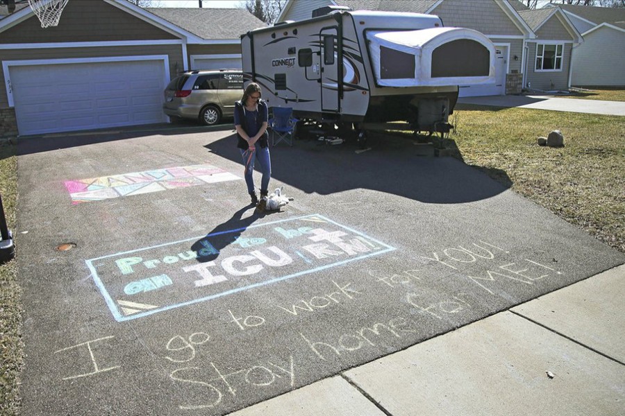 In this April 1, 2020, photo, Lisa Neuburger stands with her dog Bella by the camper she is living in and the chalk message she made in her former in-laws' driveway in St Paul Park, Minn Neuburger is living in the camper after being exposed to the coronavirus as an ICU nurse — AP photo