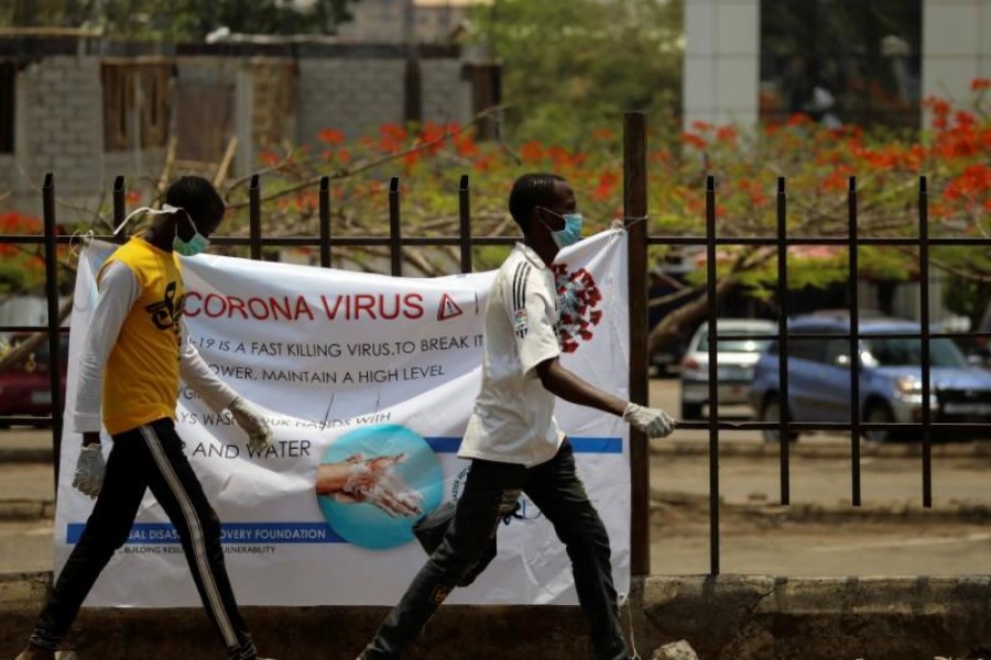Two men with protective face mask walks past a poster at Wuse market, as the authorities try to limit the spread of coronavirus in Abuja, Nigeria March 27, 2020. REUTERS/Afolabi Sotunde