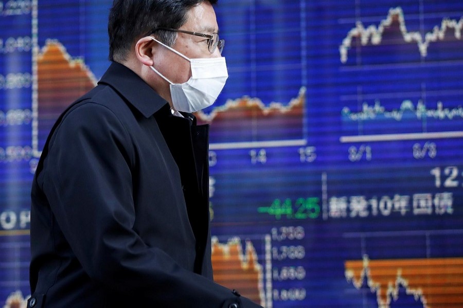A passerby wearing a protective face mask, following an outbreak of the coronavirus, walks past an electronic board showing the graphs of the recent movements of Japan's Nikkei share average outside a brokerage in Tokyo, Japan, March 06, 2020. — Reuters/Files