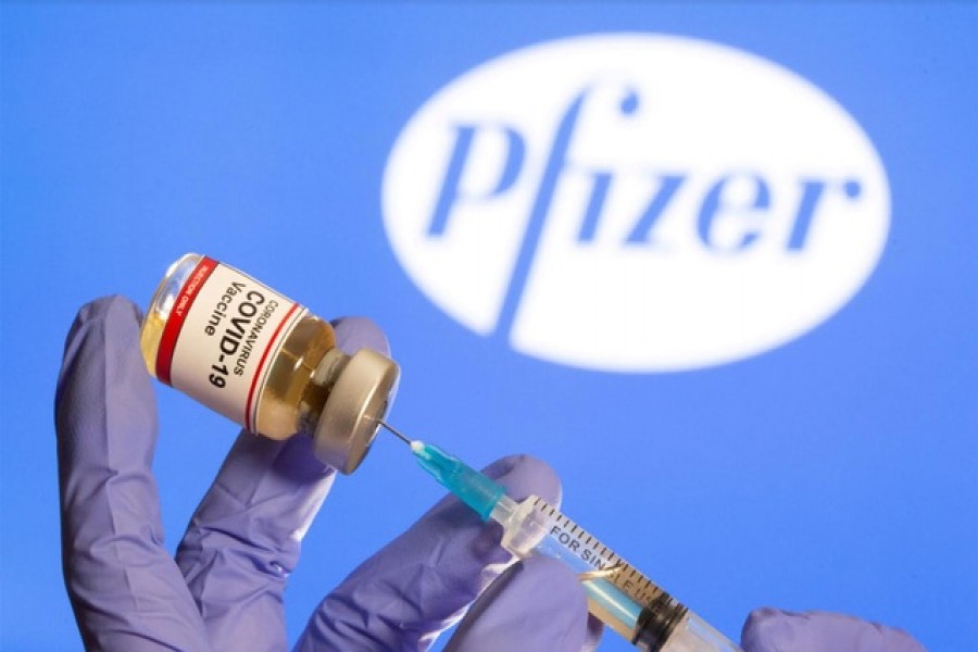 A woman holds a small bottle labeled with a "Coronavirus COVID-19 Vaccine" sticker and a medical syringe in front of displayed Pfizer logo in this illustration taken on October 30, 2020 — Reuters/Files