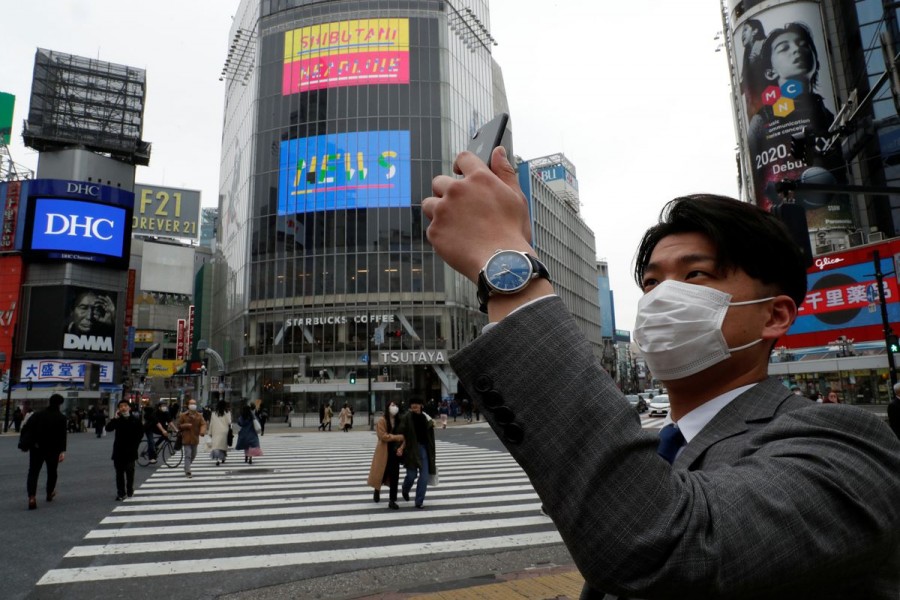 A man wearing a protective face mask, takes a photo with his mobile phone at noon, at Shibuya Crossing, during the coronavirus disease (COVID-19) outbreak, in Tokyo, Japan, March 31, 2020. REUTERS/Issei Kato