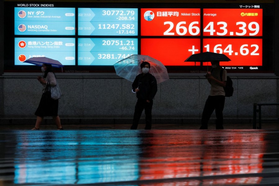Passersby wearing protective face masks walk in front of an electronic board showing Japan's Nikkei share average, amid the coronavirus disease (COVID-19) pandemic, in Tokyo, Japan July 14, 2022. REUTERS/Issei Kato