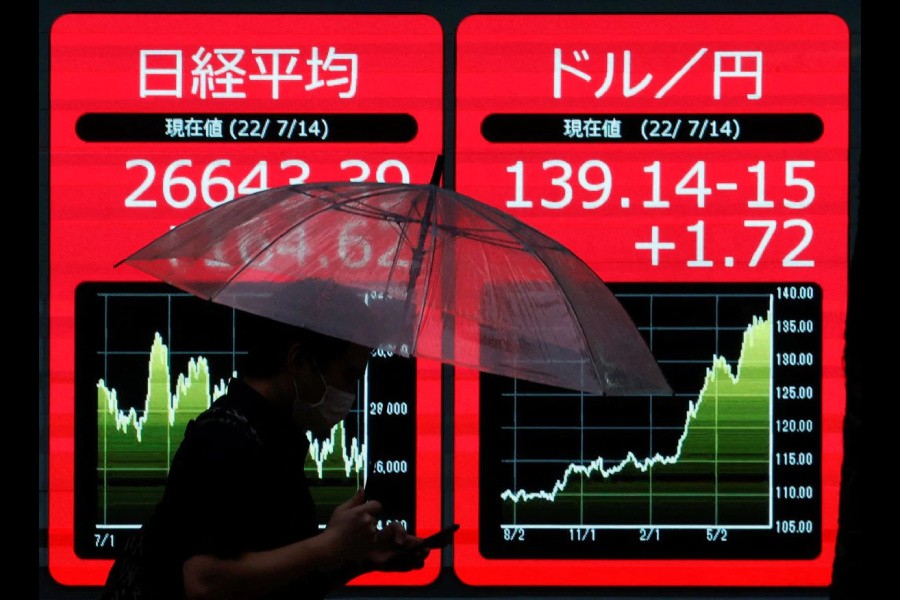 A man holding an umbrella is silhouetted as he walks in front of an electric monitor displaying the Japanese yen exchange rate against the U.S. dollar and Nikkei share average in Tokyo, Japan July 14, 2022 REUTERS/Issei Kato