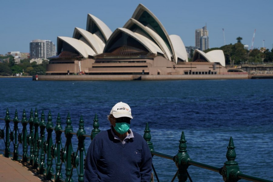 A person in protective face mask walks along the harbour waterfront across from the Sydney Opera House in Sydney, Australia, October 6, 2021. REUTERS/Loren Elliott