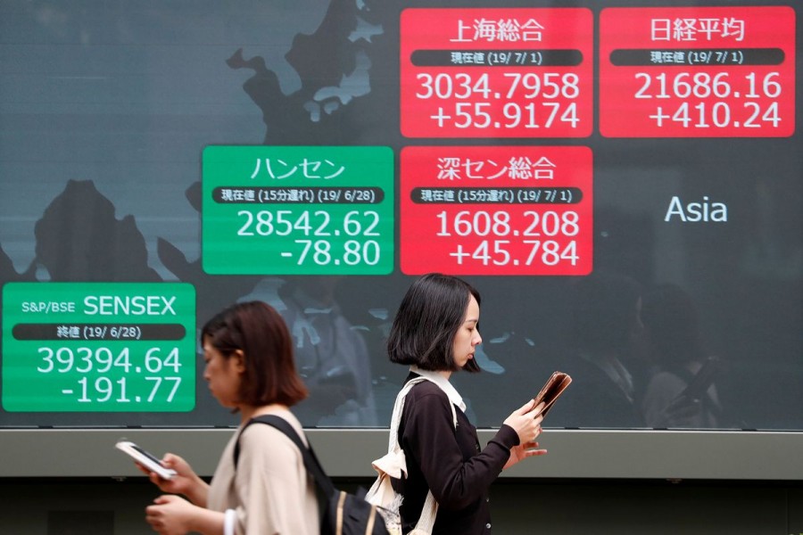 Passerbys walk past an electric screen showing Asian markets indices outside a brokerage in Tokyo, Japan, July 1, 2019. REUTERS/Issei Kato