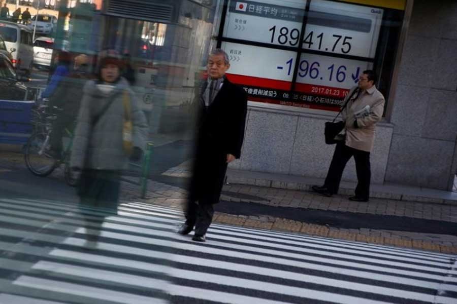 People walk past an electronic board showing Japan's Nikkei average outside a brokerage at a business district in Tokyo, Japan August 9, 2017. Reuters
