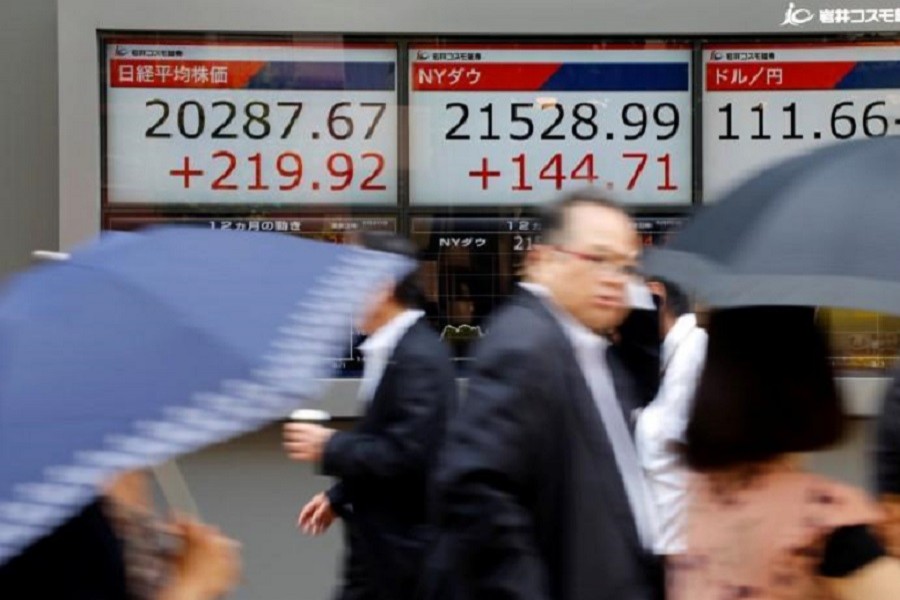 People walk past an electronic board showing Japan's Nikkei average (L), the Dow Jones average (C), and the exchange rates between the Japanese yen and the US dollar outside a brokerage in Tokyo, Japan June 20, 2017. Reuters