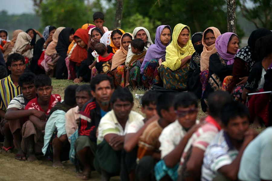 Rohingya refugees sit in a line on Tuesday as they wait to receive permission from the Bangladeshi army to continue their way after crossing the Bangladesh-Myanmar border. - Reuters photo