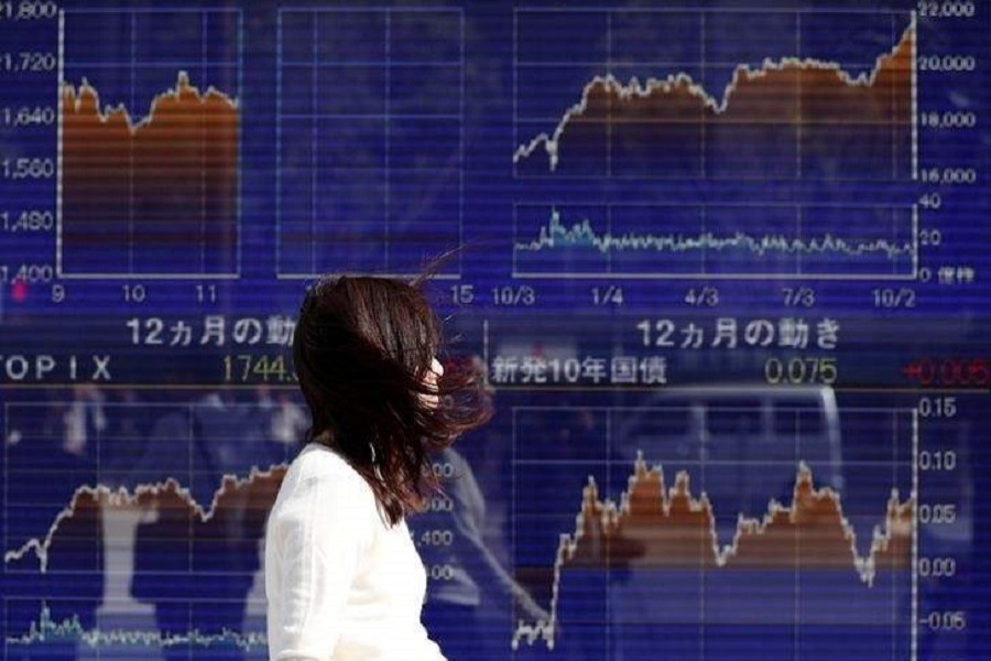 A woman walks in strong wind caused by Typhoon Lan, past an electronic board showing the graphs of the recent movements of Japan's Nikkei average outside a brokerage in Tokyo, Japan, October 23, 2017. Reuters/File Photo