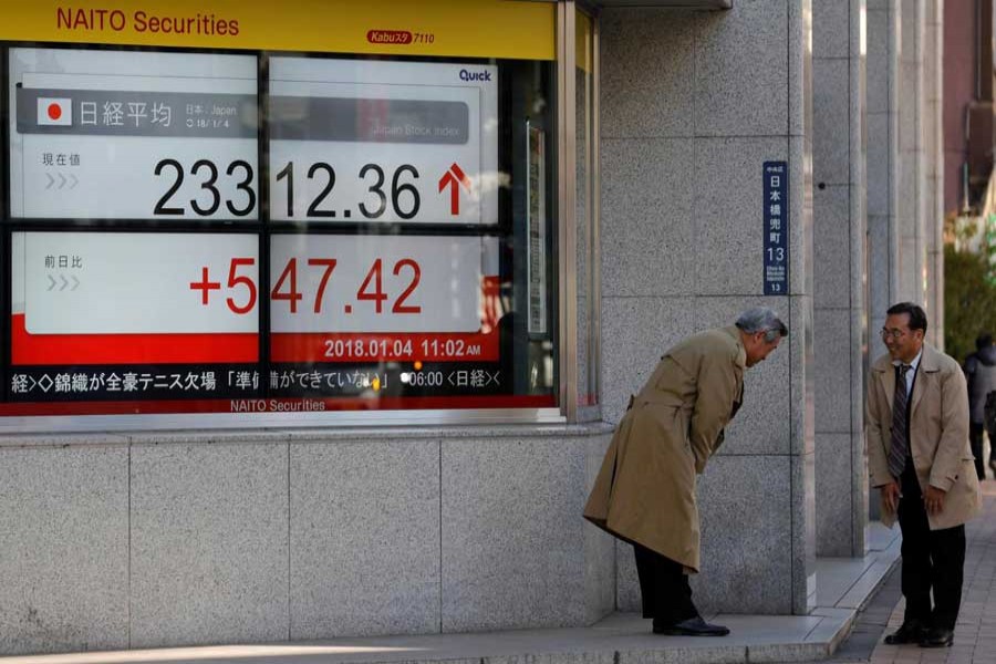 Men exchange greetings in front of an electronic board displaying the Nikkei average outside a brokerage in Tokyo, Japan, January 4, 2018. Reuters/Files