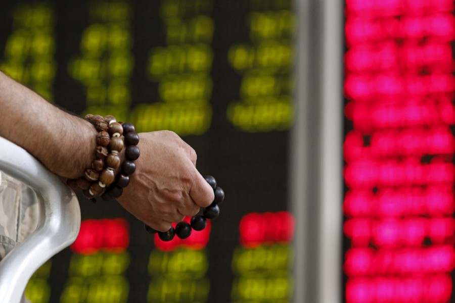 An investor holds onto prayer beads as he watches a board showing stock prices at a brokerage office in Beijing, China, July 6, 2015. Reuters/File Photo