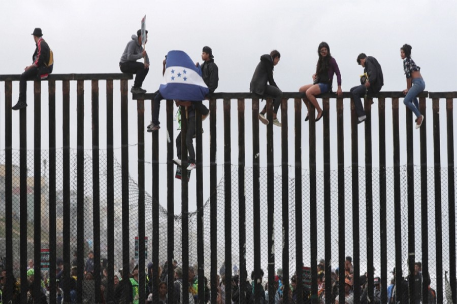 Members of a migrant caravan from Central America and their supporters sit on the top of the US-Mexico border wall at Border Field State Park before making an asylum request in San Diego, California on April 29, 2018. 	—Photo: Reuters