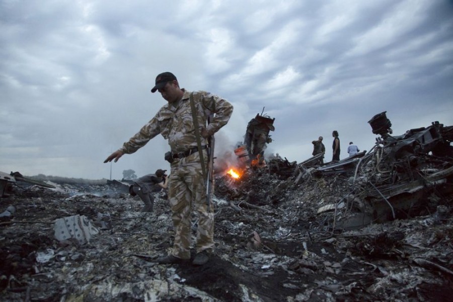 In this July 17, 2014 file photo, people walk among the debris at the crash site of a passenger plane near the village of Grabovo, Ukraine. Prosecutors investigating the downing five years ago of Malaysia Airlines Flight 17 over eastern Ukraine want to speak to a man being held by Ukrainian authorities, calling him a “person of interest” in their probe. (AP Photo/Dmitry Lovetsky, File)