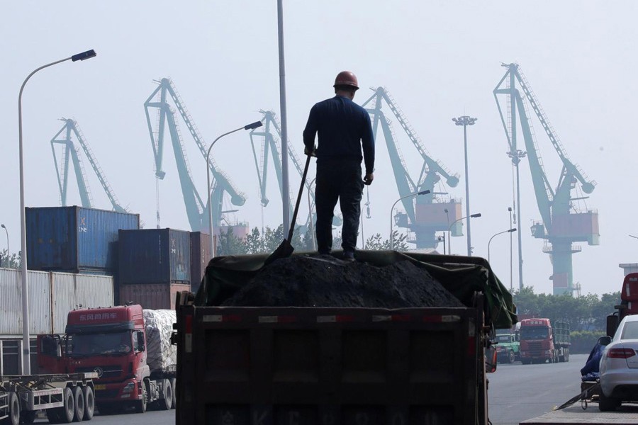 A labourer loading coal in a truck next to containers outside a logistics centre near Tianjin Port, in northern China	— Reuters