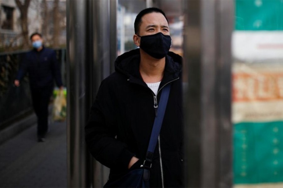 A man wearing a face mask looks at a board at a bus stop, as the country is hit by an outbreak of the new coronavirus, in Beijing, China, January 27, 2020. Reuters