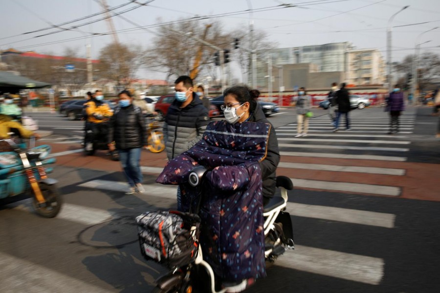 People wearing face masks ride their scooters and walk on a street following an outbreak of the coronavirus disease (COVID-19), in Beijing, China March 30, 2020. REUTERS/Carlos Garcia Rawlins