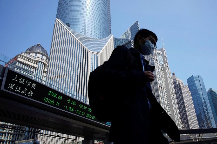 A pedestrian wearing a face mask walks near an overpass with an electronic board showing stock information, following an outbreak of the coronavirus disease (COVID-19), at Lujiazui financial district in Shanghai, China, March 17, 2020. — Reuters/Files