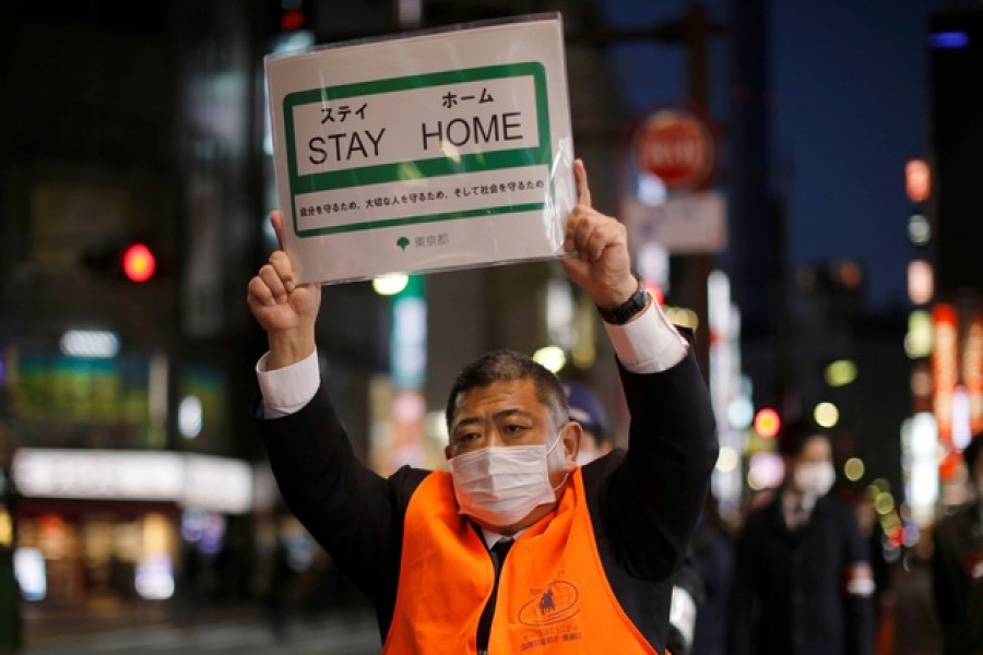 A staff members of the Tokyo metropolitan government wearing a protective face mask shows off a placard as he calls for people to stay home after the government announced the state of emergency for the capital and some prefectures following the coronavirus disease (COVID-19) outbreak, at an entertainment and amusement district in Tokyo, Japan Apr 14, 2020. REUTERS