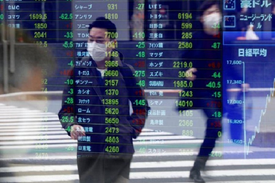 Passersby wearing protective face masks following an outbreak of the coronavirus disease (COVID-19) are reflected on a screen displaying stock prices outside a brokerage in Tokyo, Japan, March 17, 2020. —Reuters