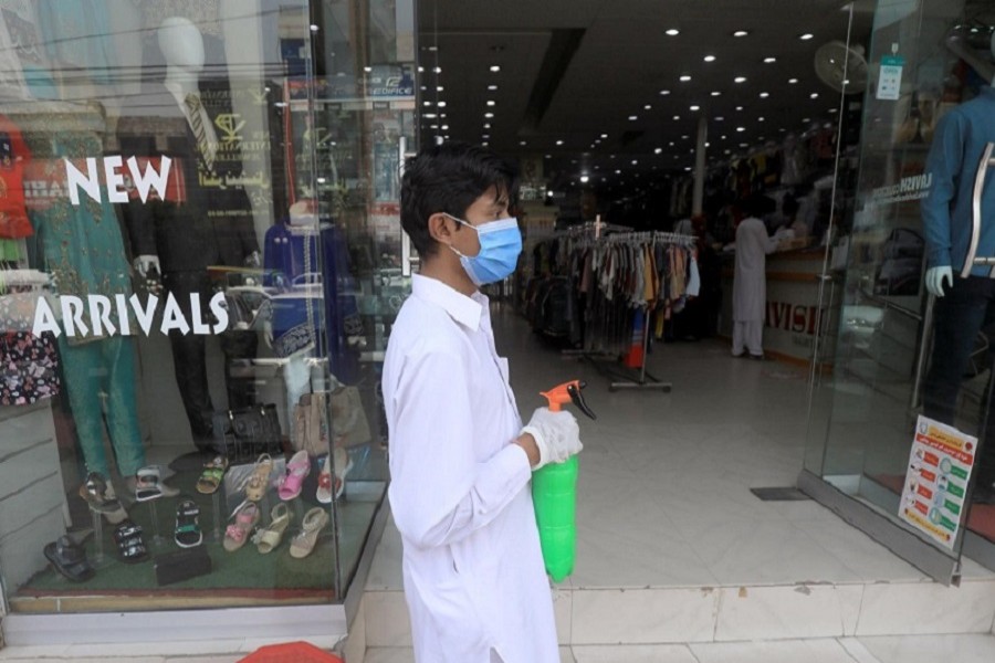 A worker wearing a protective face mask and gloves holds a spray bottle to disinfect customers outside a shop in a market, after Pakistan started easing lockdown as the coronavirus disease (COVID-19) continues, in Peshawar, Pakistan May 11, 2020. — Reuters/Files