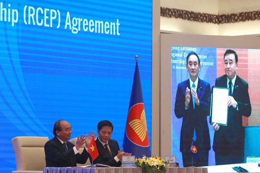 Vietnamese Prime Minister Nguyen Xuan Phuc, left, and Minister of Trade Tran Tuan Anh, right, applaud next to a screen showing Japanese Prime Minister Yoshihide Suga and Minister of Trade Hiroshi Kajiyama holding up the signed RCEP agreement, in Hanoi, Vietnam, November 15, 2020 — AP