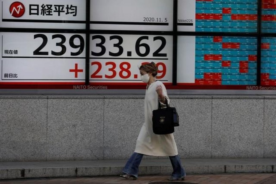 A woman wearing a protective mask, following the coronavirus disease (Covid-19) outbreak, walks past a screen showing Nikkei index outside a brokerage in Tokyo, Japan on November 5, 2020 — Reuters/Files