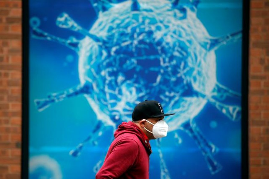 FILE PHOTO: A man wearing a protective face mask walks past an illustration of a virus outside a regional science centre, as the city and surrounding areas face local restrictions in an effort to avoid a local lockdown being forced upon the region, amid the coronavirus disease (COVID-19) outbreak, in Oldham, Britain August 3, 2020. REUTERS/Phil Noble