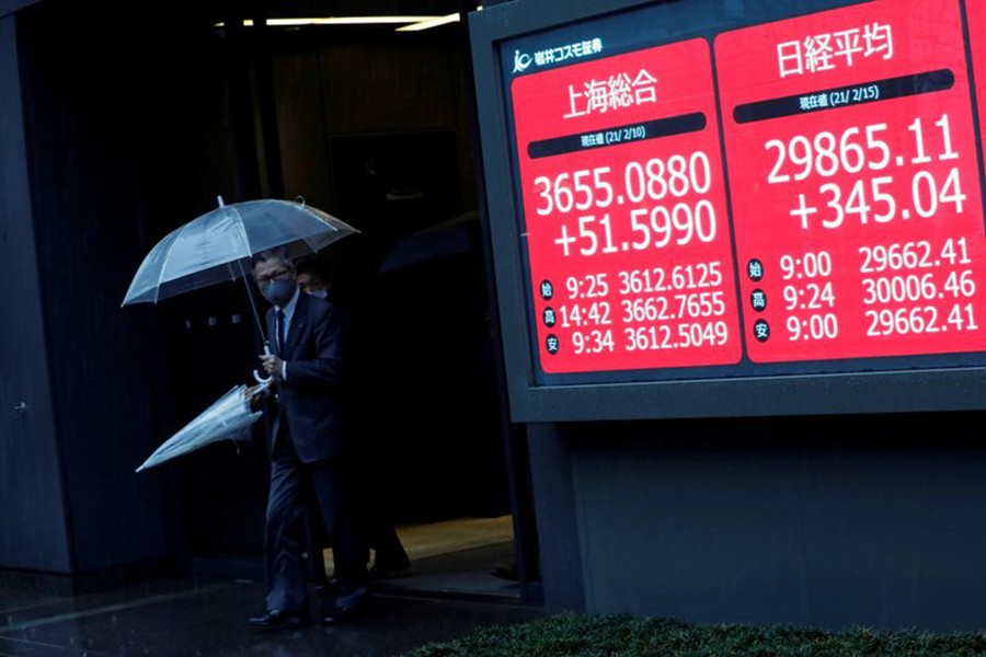 Men holding umbrellas walk near an electric board showing Nikkei index at a brokerage in Tokyo, Japan on February 15, 2021 — Reuters photo