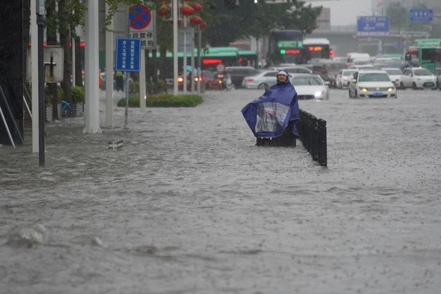 A resident wearing a rain cover stands on a flooded road in Zhengzhou, Henan province, China July 20, 2021 — cnsphoto via Reuters