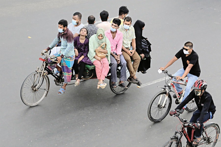 A group of people are travelling on a rickshaw van while two others are riding bicycles to their destinations. People who have to come out due to emergency rely on these modes of transport during the ongoing lockdown. The photo was taken in the Rayerbagh area on the Dhaka-Chattogram highway on Thursday — FE photo by Shafiqul Alam