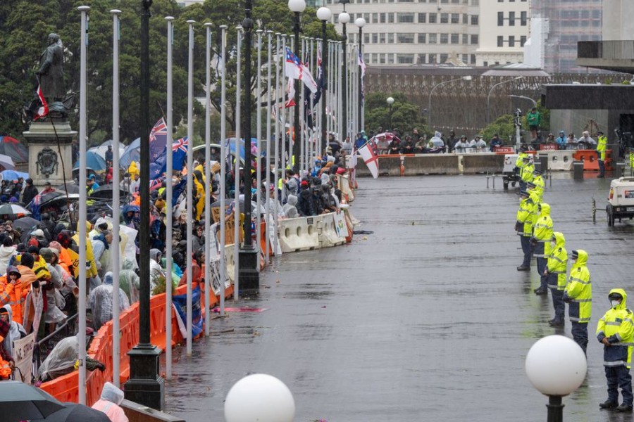 Police stand guard in front of protestors rallying against coronavirus disease (COVID-19) vaccination mandates despite the rain, near the parliament building in Wellington, New Zealand February 13, 2022 in this picture obtained from social media. Courtesy Charlie Coppinger/via REUTERS