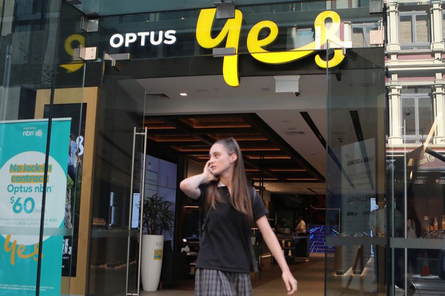 A woman uses her mobile phone as she walks past in front of an Optus shop in Sydney, Australia on February 8, 2018 — Reuters/Files